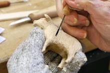 Photo of a hand carving a small cow from wood